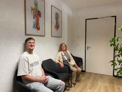 Zwei Personen sitzen in einem Wartebereich mit bunten Kunstwerken an der Wand.