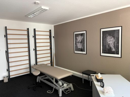 Behandlungsraum mit einem Therapietisch, einem Stuhl und zwei Bildern an der Wand.