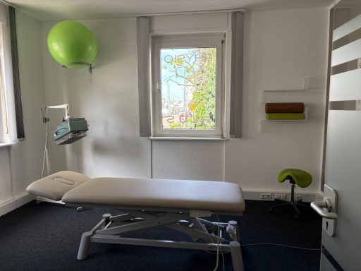 Behandlungsraum mit einer Liege, einem Wandgerät und einem grünen Gymnastikball.